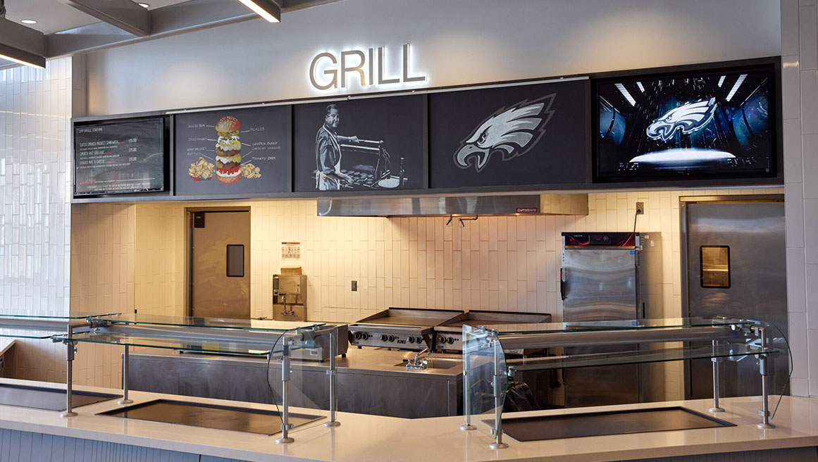a kitchen and grill station with BrightSign digital signage playing on screens above industrial fan
