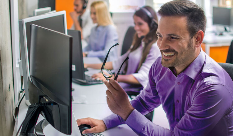 Glimlachende BrightSign customer support agent die bril afneemt en aan computer werkt