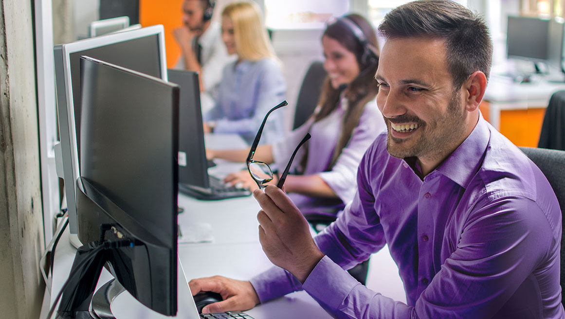Sorridente BrightSign agente di assistenza clienti che si toglie gli occhiali e lavora al computer