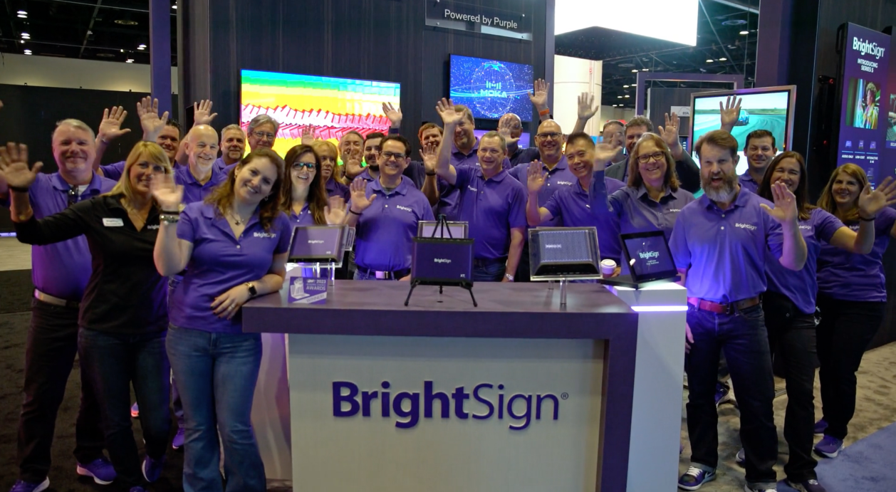 BrightSign team waving at infocomm 23 table