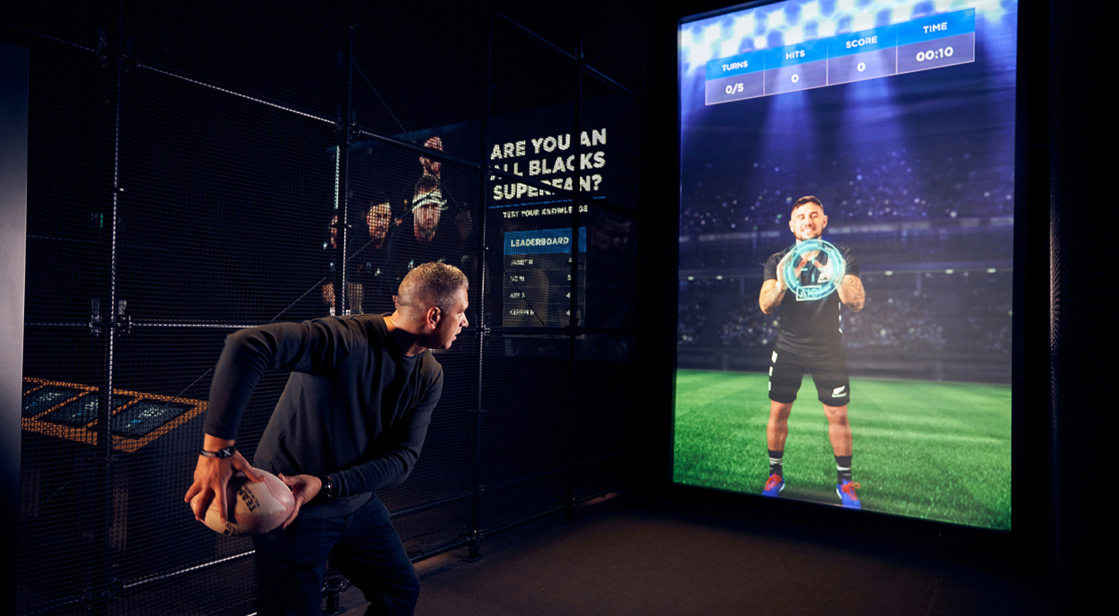 man tossing a rugby ball into an interactive screen at the All Blacks Experience powered by BrightSign digital signage players