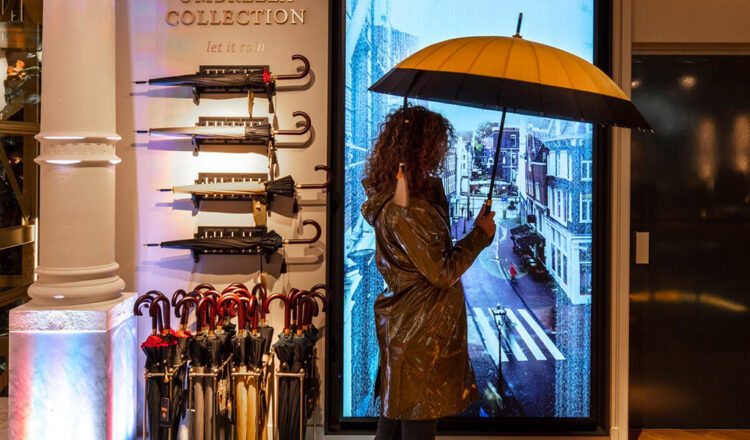 Woman holding an umbrella in front of a digital retail display