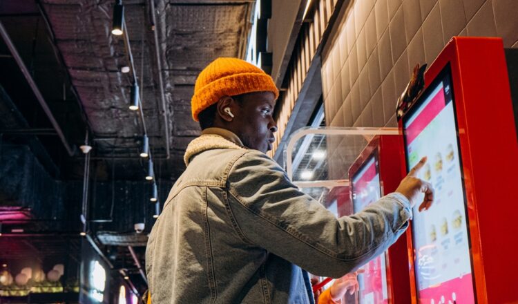 Profile shot of an African American man with his right hand extended towards a touchscreen kiosk with a digital menu